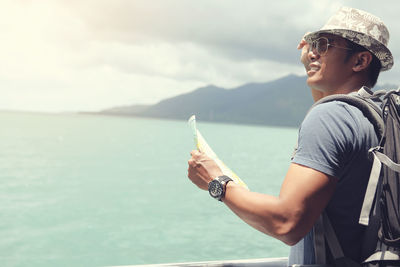 Side view of man holding sea against sky
