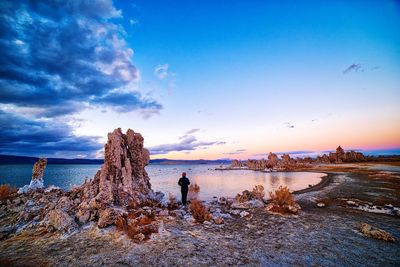 Woman standing at beach against sky during sunset