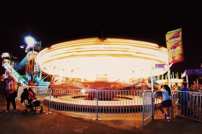 People at illuminated amusement park against sky at night