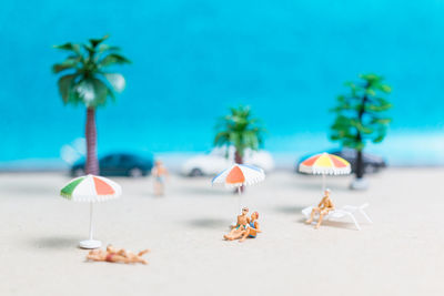 Miniature people wearing swimsuit relaxing on the beach with blue background