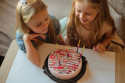 Little twin girls, children blow out candles cake birthday party at home. holiday during quarantine