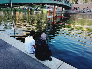 Rear view of people sitting by lake