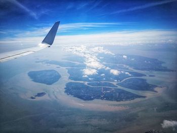 Aerial view of airplane wing over landscape against blue sky