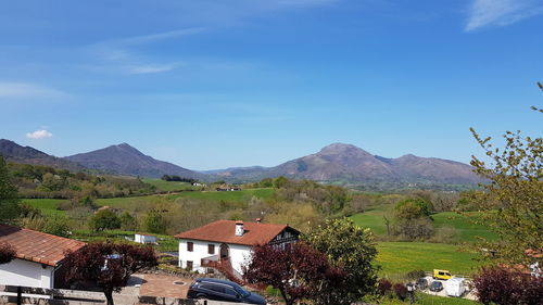 Houses by trees and mountains against blue sky