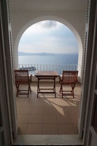 Chairs by sea against sky seen through window