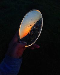 Close-up of hand holding wet mirror with orange sky reflection