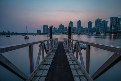 Pier at lake against sky during sunset in city