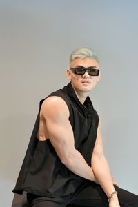 Young man wearing sunglasses sitting against wall