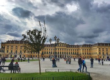 Tourists in front of historical building against cloudy sky