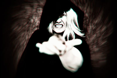 Close-up portrait of woman with hand on black background