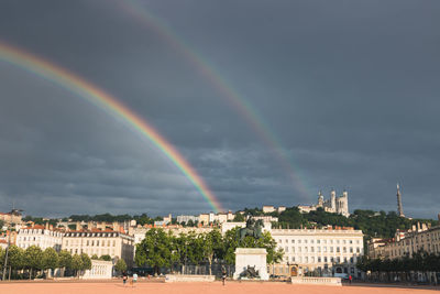 Rainbow over buildings in city of lyon, bellecour square against sky