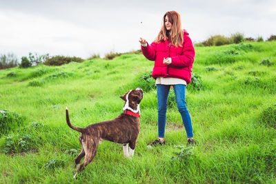 Full length of woman playing with dog standing on field