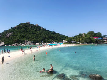 People enjoying at beach against clear blue sky