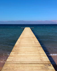 Pier over sea against clear blue sky