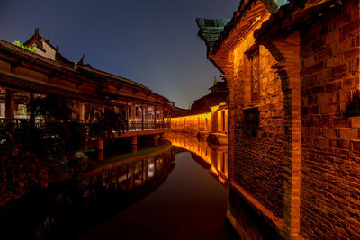 Illuminated canal amidst buildings against sky at night