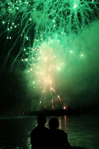 Rear view of people watching firework display at night