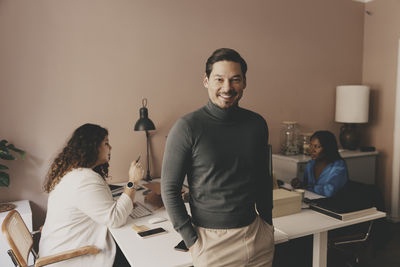 Portrait of smiling businessman standing near desk with female colleagues working at office