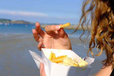 Close-up of woman holding food at beach against sky