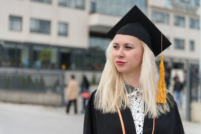 Portrait of woman wearing graduation gown standing outdoors