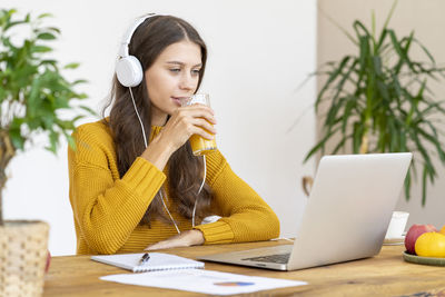 Young girl with headphones talking on conference calls,drinking orange juice, smiling.