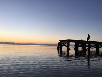 Silhouette person standing on pier over sea against clear sky during sunset