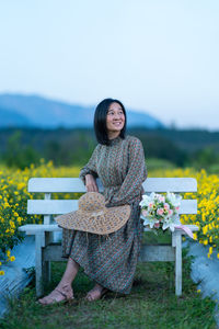 Portrait of young woman sitting on seat against plants