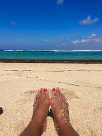 Low section of woman on beach against blue sky