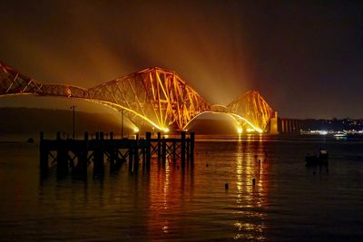 Illuminated bridge over river in city at night