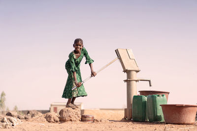 Full length portrait of girl using water pump on land