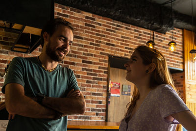 Smiling young couple standing in cozy bar and talking each other