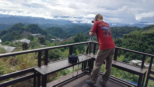 Rear view of man standing on railing against mountain