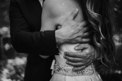 Midsection of wedding couple embracing while standing outdoors