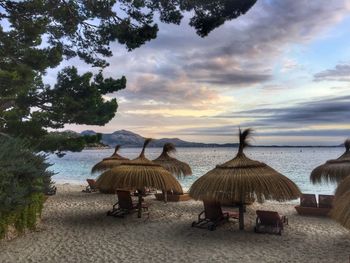 Chairs on beach against sky during sunset