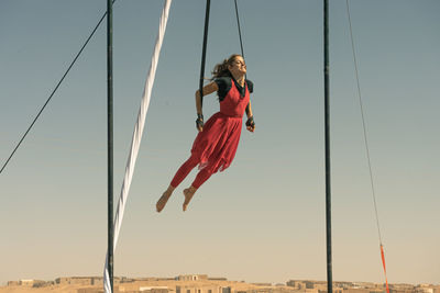 Full length of female aerial dancer dancing while hanging from textile against sky