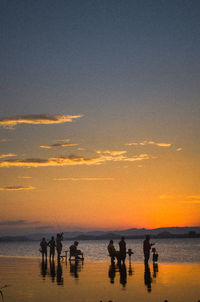 Silhouette people on beach against sky during sunset