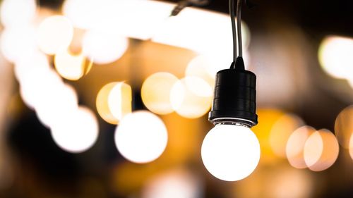 Close-up of illuminated light bulb hanging from ceiling