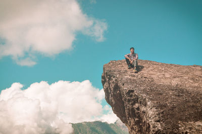 Low angle view of man sitting on rock against sky