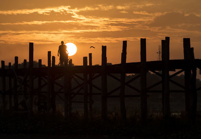 Silhouette man standing by railing against sky during sunset