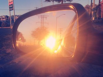 Close-up of side-view mirror against sunset sky