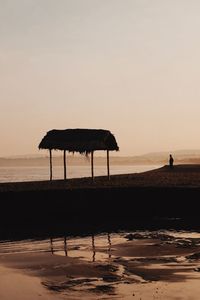 Thatched roof hut against sky during sunset at beach