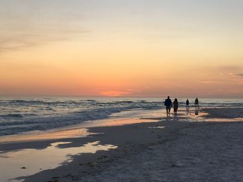 Silhouette people on beach against sky during sunset