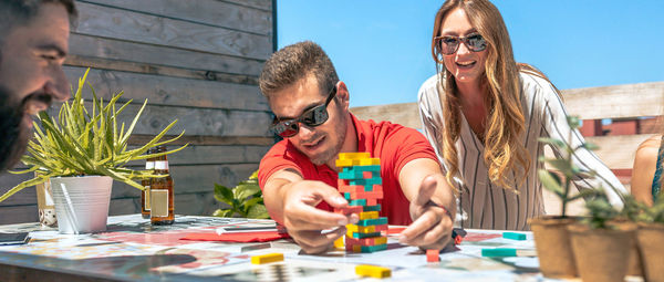 Concentrated man catching jenga game piece next to colleagues on terrace