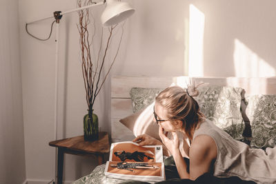 Portrait of young woman sitting on table against wall at home