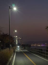 Illuminated street lights on road against sky at night