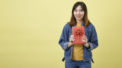 Portrait of smiling young woman standing against yellow background
