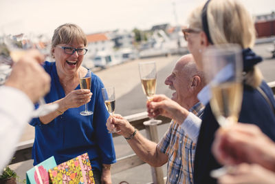 Cheerful senior woman toasting champagne flute with friends on restaurant patio