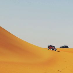 Cars on sand in desert against clear sky