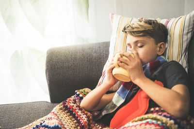 Boy drinking coffee while resting on sofa at home