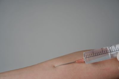 Close-up of cropped hand injecting syringe against gray background