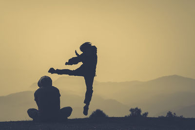 Silhouette person exercising by friend on field